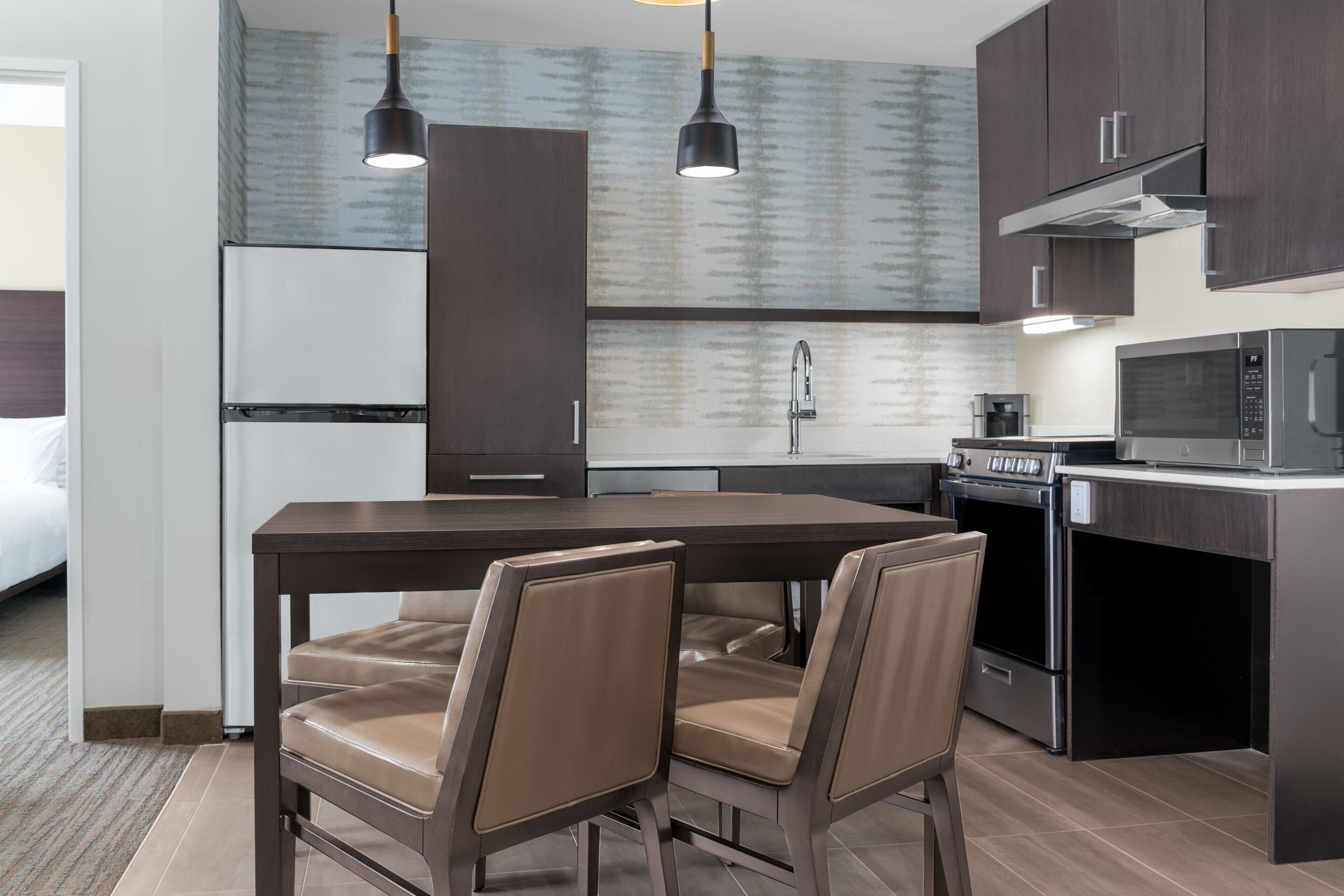 A modern kitchen with dark cabinetry, a central island with chairs, a microwave, and an oven.