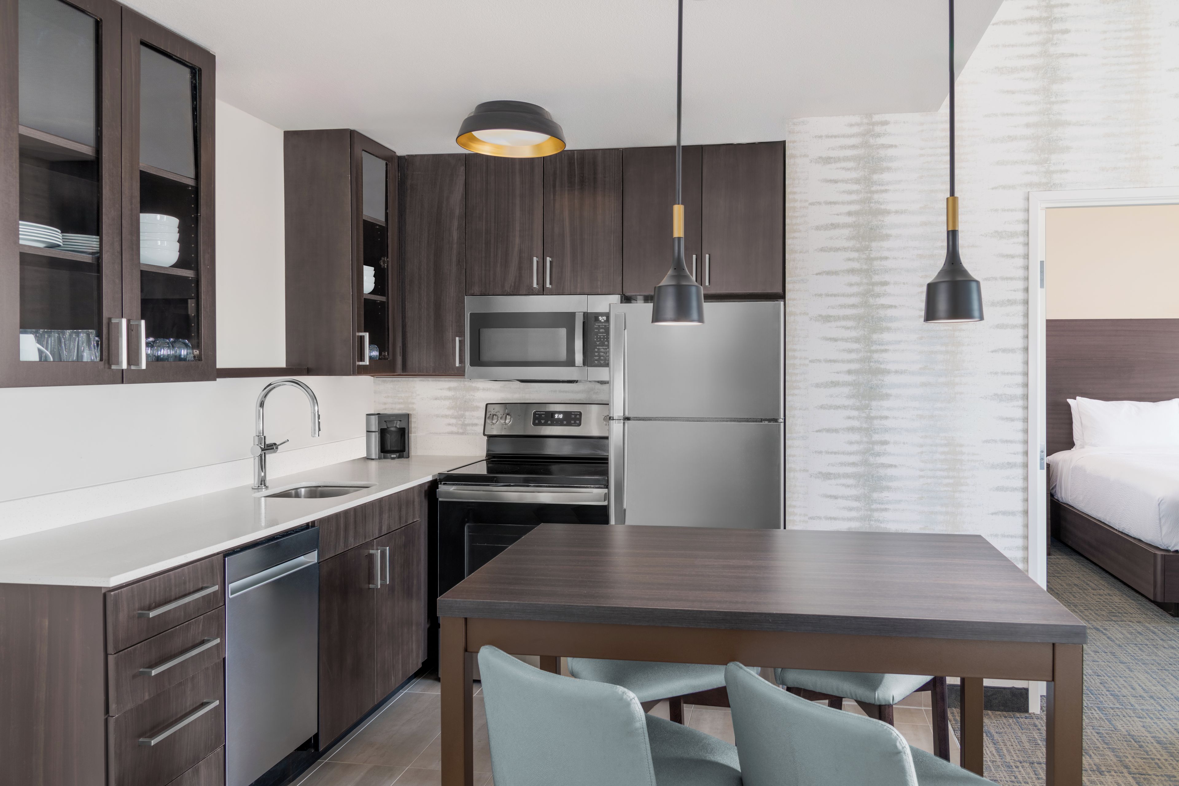 A modern kitchen with dark wood cabinets, stainless steel appliances, and a dining area with a table and chairs.