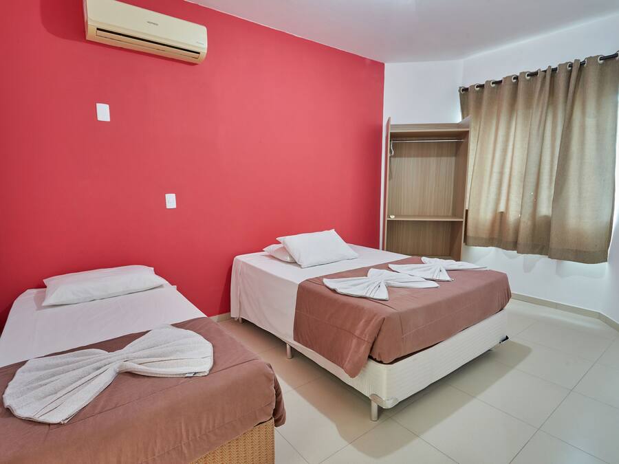 Una habitación de hotel con dos camas, paredes rojas, un armario y una ventana con cortinas.