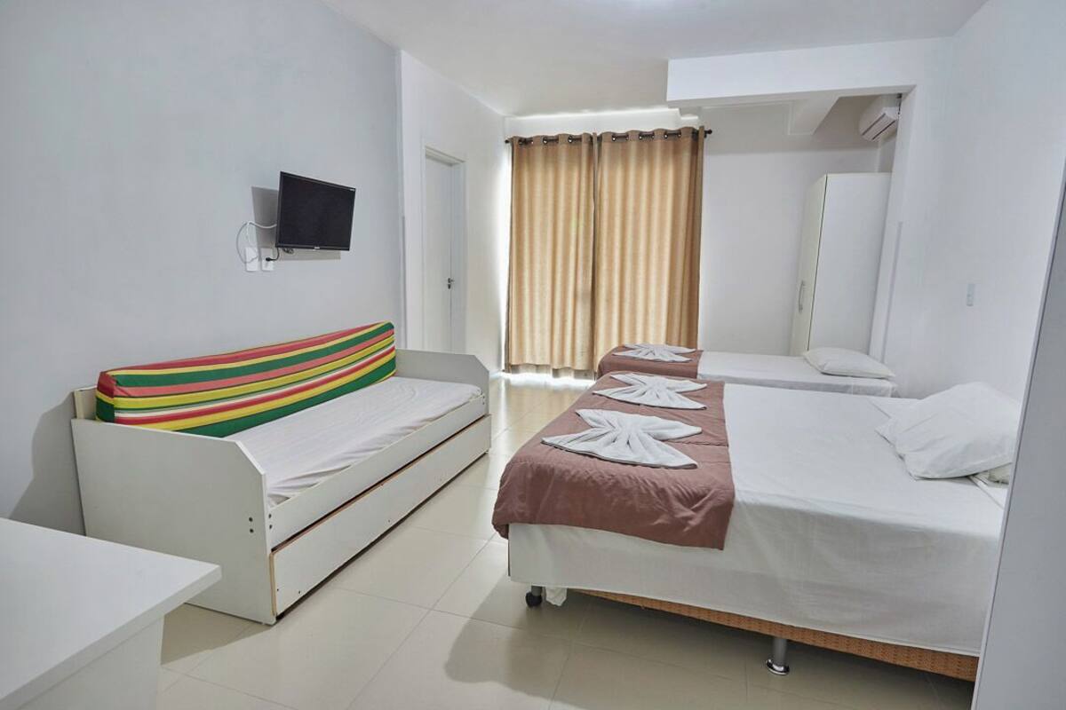 A hotel room with a single bed, a sofa bed, a TV mounted on the wall, and a window with curtains.