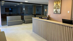 A modern reception area with a wooden reception desk, a sofa, and a glass partition. - Hotel Monte Libano (Florianópolis)