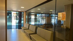 A hotel lobby with a seating area, a reception desk, and a view of the street outside. - Hotel Monte Libano (Florianópolis)
