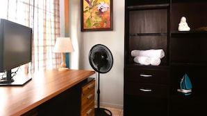 A room with a wooden desk, a black standing fan, a wall-mounted painting, a dark wooden wardrobe, and a small white figurine. - Papaya Dreams (San Juan)