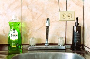 A bathroom sink with a green bottle of liquid soap, a faucet, and a black bottle of hand sanitizer. - Papaya Dreams (San Juan)