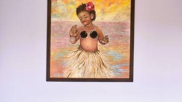 A framed painting of a woman in a tropical dress on a wall above a black leather sofa with two red cushions.