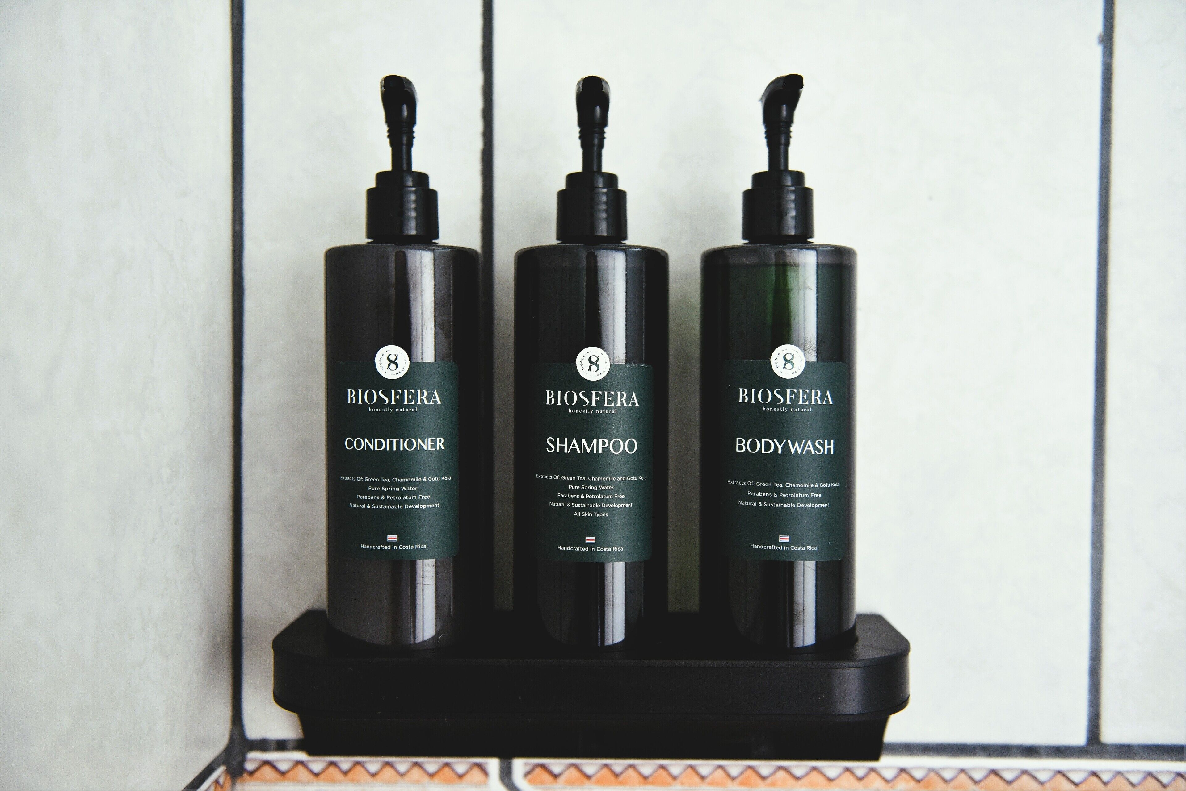 Tres botellas de productos Biosfera sobre una bandeja negra frente a una pared de azulejos.