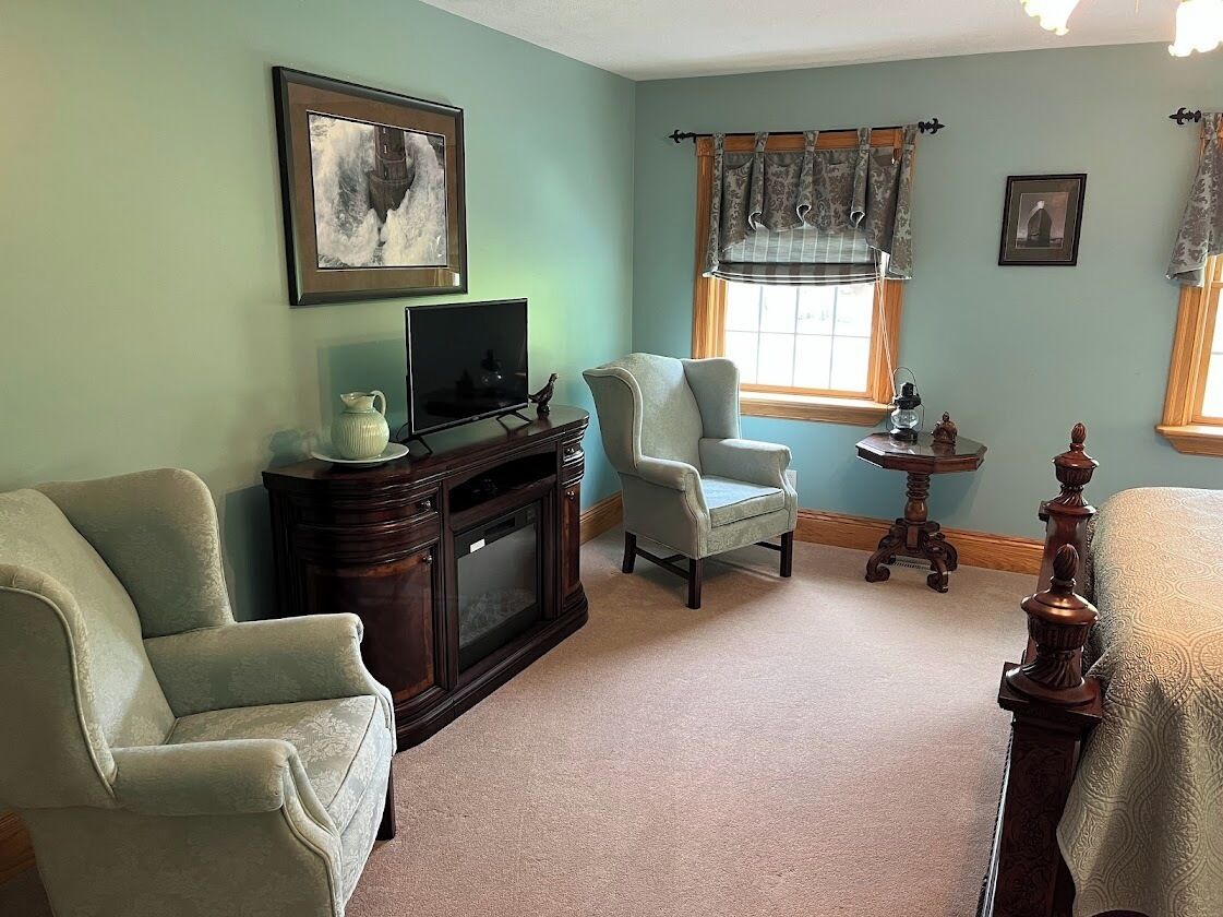 A living room with a fireplace, a television, two armchairs, a small table, and a window with curtains.