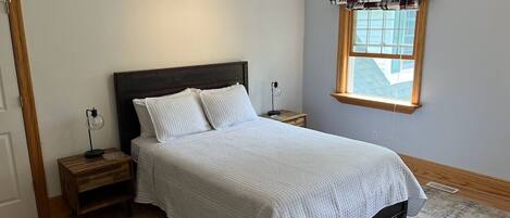 A bedroom with a bed, wooden nightstands, a window with a view, and a ceiling fan.