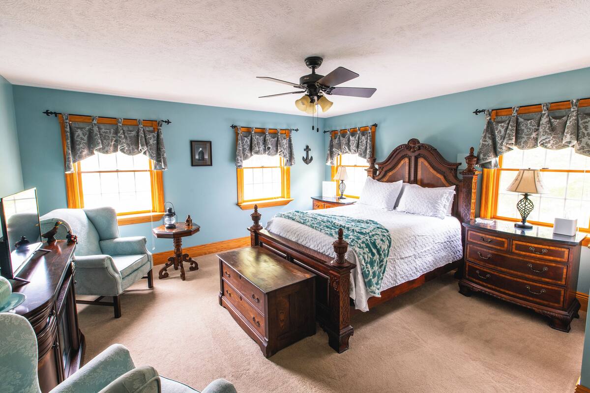 A bedroom with a bed, dresser, chair, desk, and a ceiling fan.