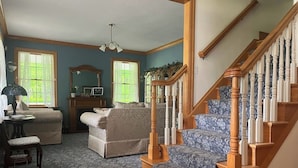 A spacious living room with a wooden staircase, a fireplace, and a large window. - The Inn at Woodsong Acres (Kingsville)