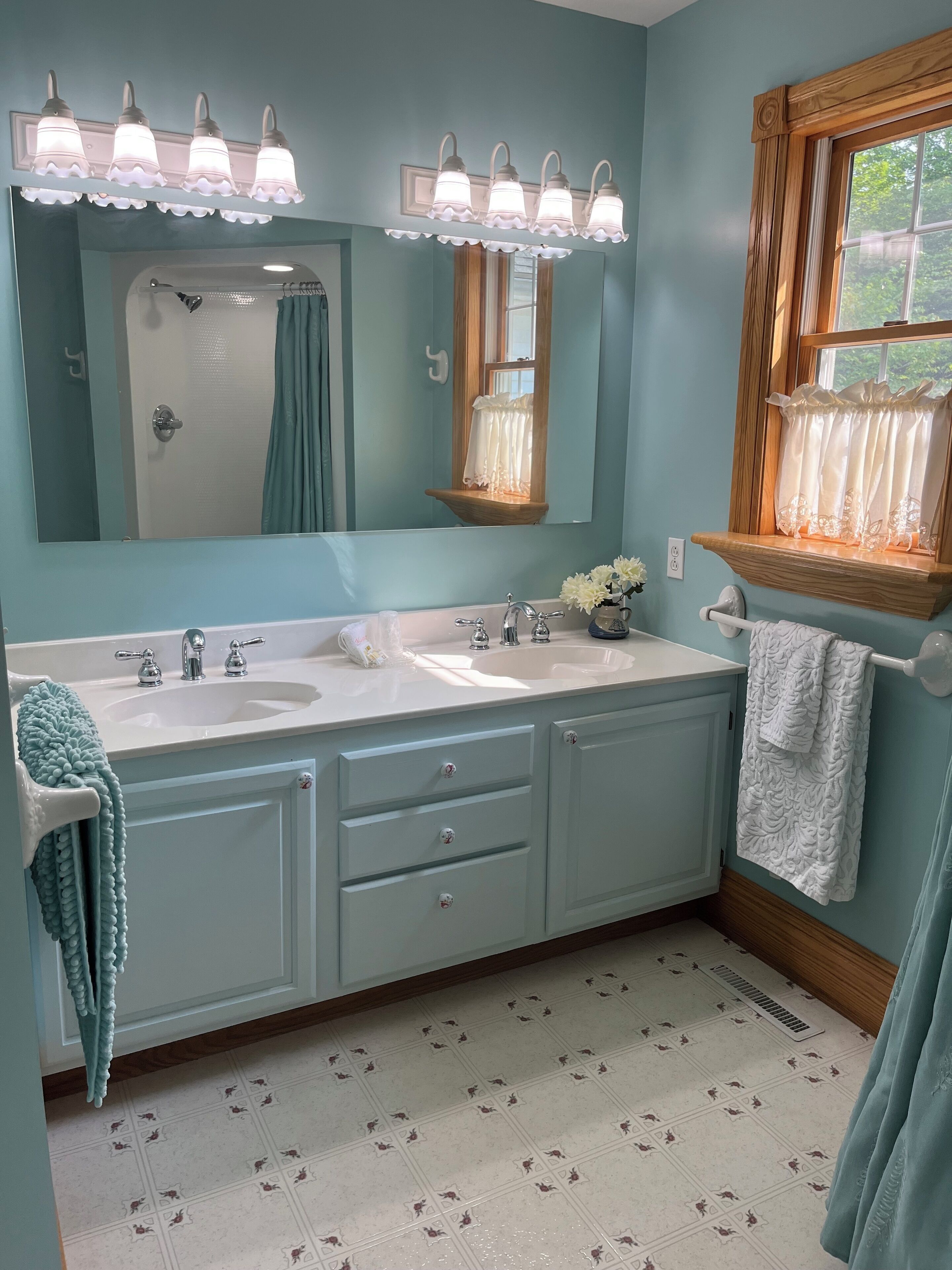 A bathroom with two sinks, a large mirror, and a window with a wooden frame.