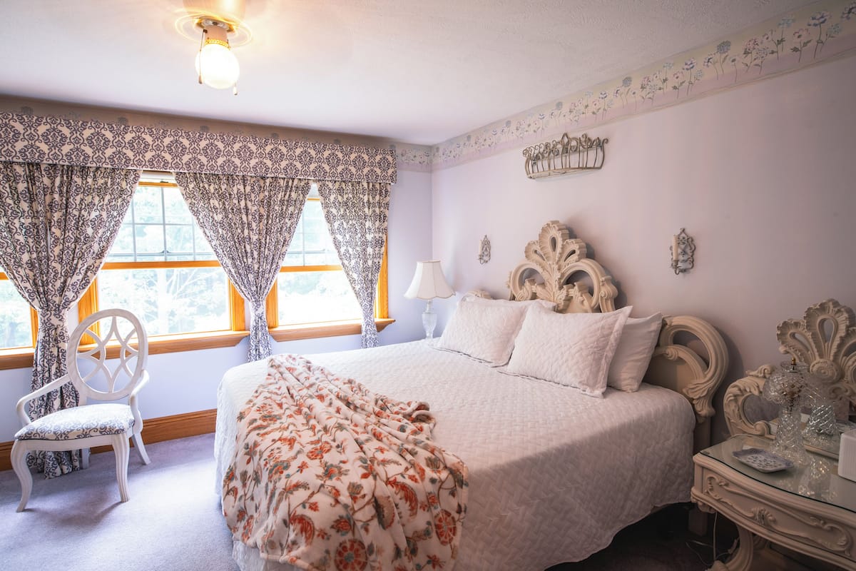A bedroom with a bed, a chair, a nightstand, and a lamp.