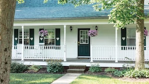 A white house with green shutters, a dark green front door, and a porch with white railings. - The Inn at Woodsong Acres (Kingsville)