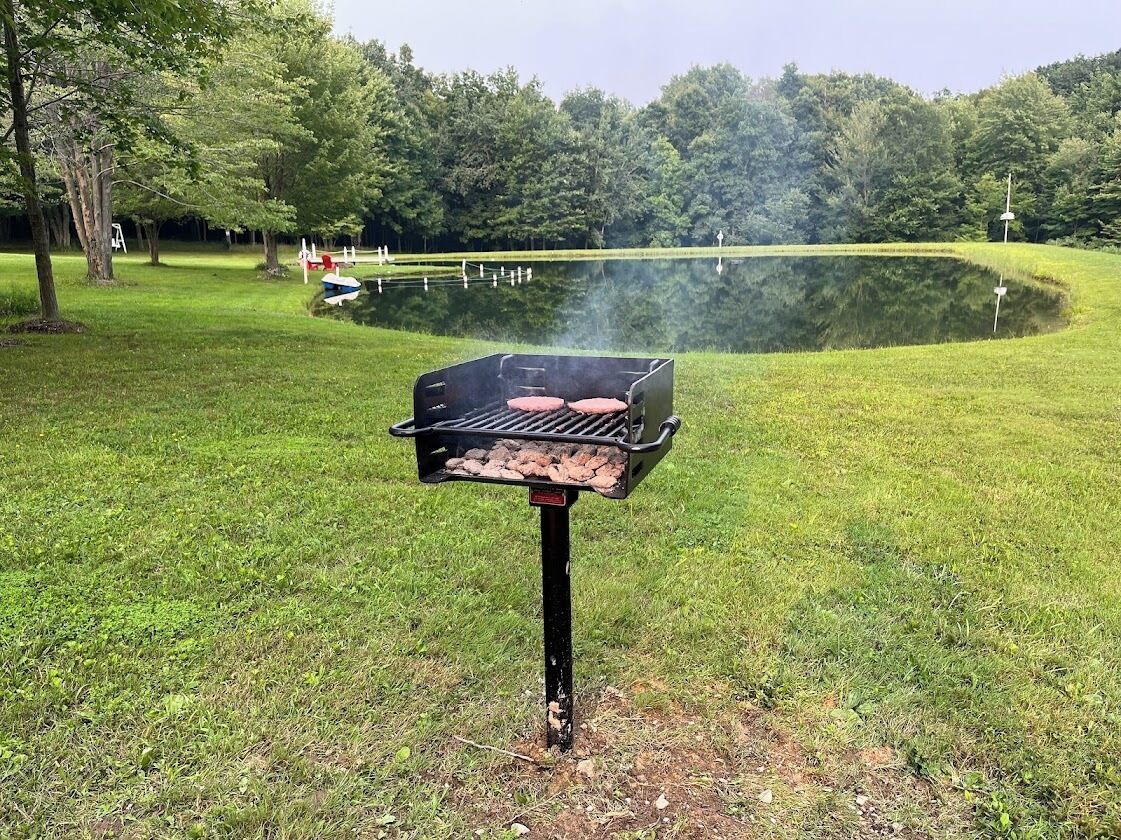 En grill där man grillar kött utomhus, omgiven av en gräsyta och en damm.