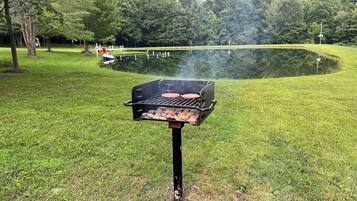 En grill där man grillar kött utomhus, omgiven av en gräsyta och en damm.