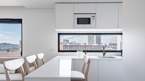 Eine moderne Küche mit integriertem Mikrowellenherd, einem großen Fenster mit Blick auf die Stadt und einem Essbereich mit einem langen Tisch und Stühlen.