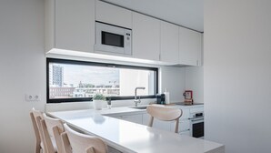 Eine moderne Küche mit großem Fenster, weißen Schränken, einer Bosch-Mikrowelle und einem Essbereich mit Holzkohle.
