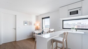 Eine moderne Küche mit weißen Schränken, einer zentralen Kochinsel und Blick auf die Stadt durch ein großes Fenster.