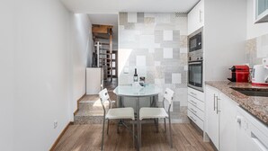 Una cocina moderna con una mesa redonda, sillas blancas, horno empotrado y una cafetera roja.