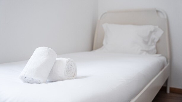 Una cama individual con ropa blanca y dos toallas enrolladas encima.