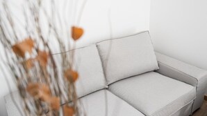 Un sofá de gris claro con un cojín, colocado frente a una pared lisa.