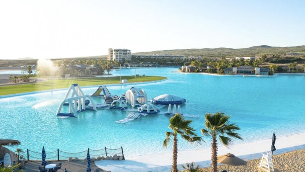 A resort with a large pool, palm trees, and a building in the background. - Chasing Sunsets in Cabo - Pacific Ocean Beachfront 1B/1B Luxury Junior Suite (Cabo San Lucas)