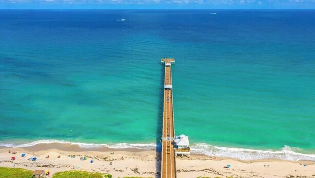 A pier extending into the ocean with a beach and a lifeguard tower at the end.