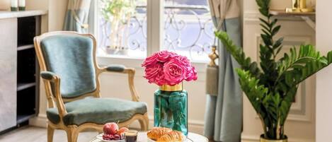 A dining table with a vase of flowers, a plate of fruit, a croissant, and a cup of coffee.