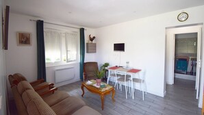 A living room with a sofa set, a dining table with chairs, a television, and a window with curtains. - Appartement à Caudecoste, proche d'Agen (CAUDECOSTE)