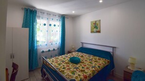 A bedroom with a bed, a wardrobe, a window with curtains, a bedside table, and a painting on the wall. - Appartement à Caudecoste, proche d'Agen (CAUDECOSTE)