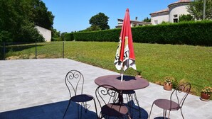 An outdoor patio with a round table and two chairs, a red umbrella, and a building in the background. - Appartement à Caudecoste, proche d'Agen (CAUDECOSTE)