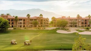 Un campo de golf con un club de campo y montañas al fondo.
