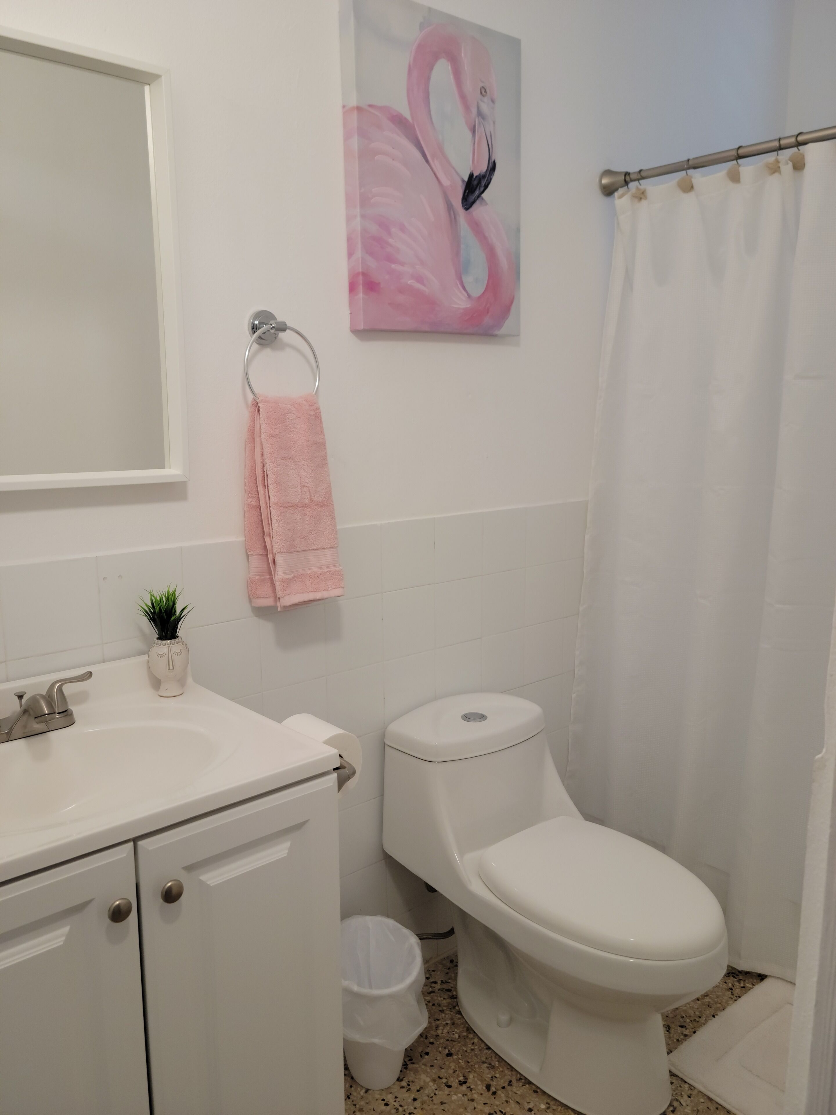 Une salle de bain avec un lavabo blanc, des toilettes, un tableau représentant un flamant rose et un rideau de douche.