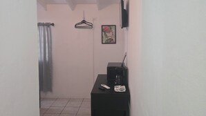 A narrow hallway with a tiled floor, a black desk with a coffee maker, a framed picture, and a wall-mounted TV. - HighTide Guesthouse (La Parguera)