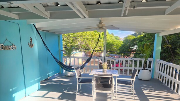 A covered outdoor area with a table and chairs, a hammock, and a view of greenery. - HighTide Guesthouse (La Parguera)