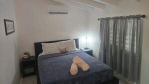 A bedroom with a bed, a nightstand, an air conditioner, a lamp, and a window with curtains. - HighTide Guesthouse (La Parguera)