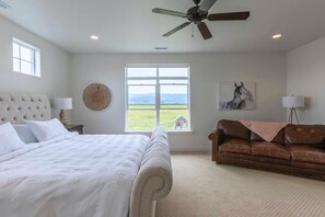 Quarto com uma cama grande, um sofá de couro marrom, uma janela com vista e um ventilador de teto.