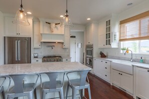 A modern kitchen with white cabinets, stainless steel appliances, a marble countertop, and pendant lighting. - Hearthstone Farm - Great Teton Views (Driggs)