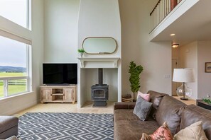 A spacious living room with a fireplace, a television, and a large window offering a view of the outdoors.