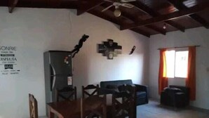 Un comedor con una mesa y sillas de madera, un refrigerador y una ventana con cortinas.