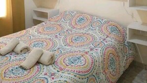 Un dormitorio con cama, ropa de cama estampada, un armario con estantes múltiples y un perchero.