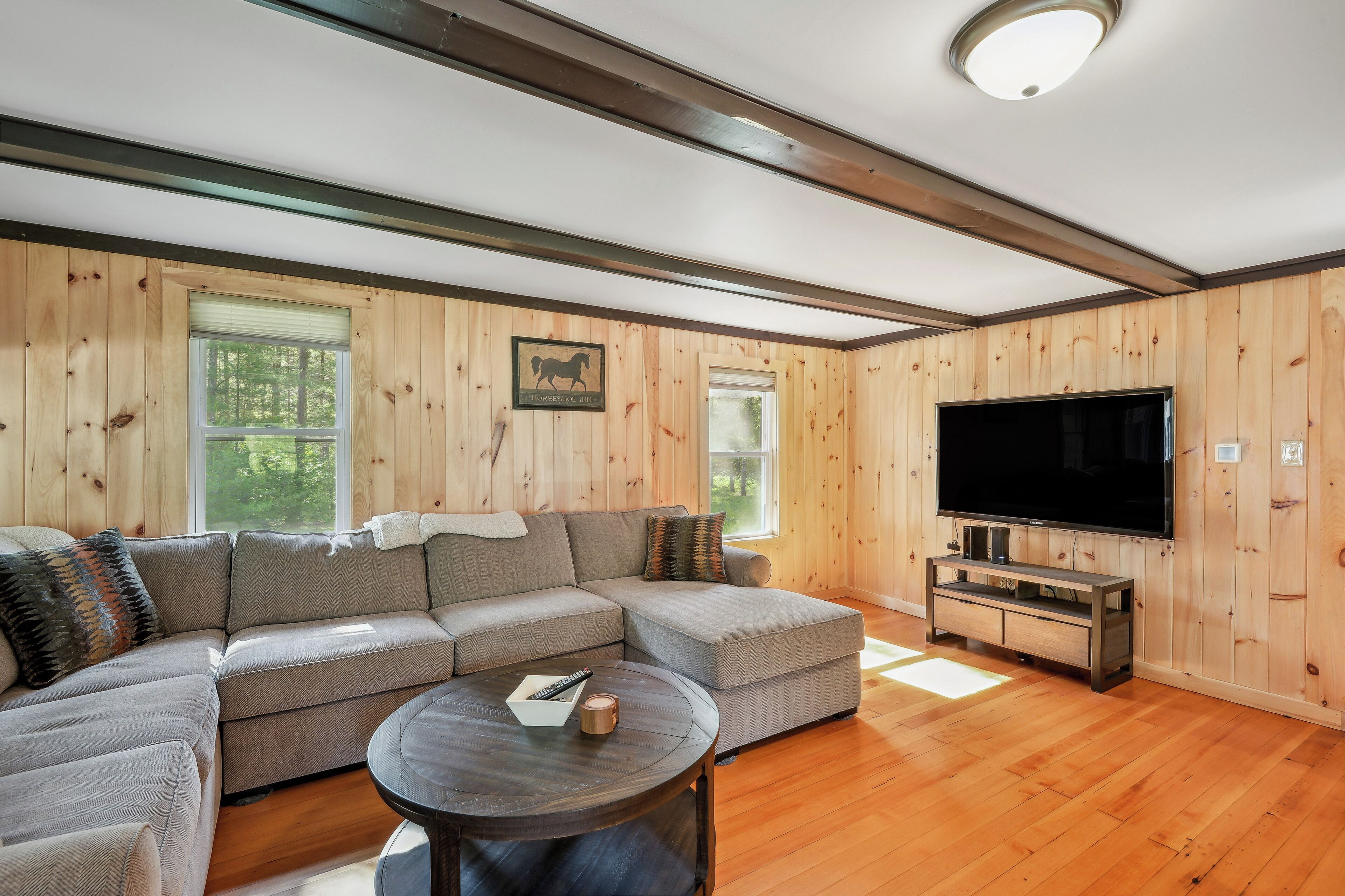 A modern living room with a sectional sofa, a flat-screen TV, and wooden walls.
