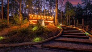 Um deck de madeira com luzes de corda, rodeado por uma floresta.