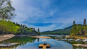 Um lago tranquilo com barcos atracados, um píer de madeira e montanhas ao fundo.