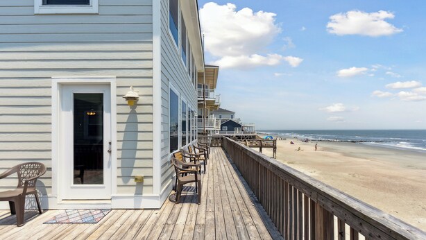 A wooden deck with a view of the beach, a door, and a chair.