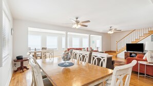 A spacious living room with a wooden dining table, white chairs, a red sofa, and a staircase.