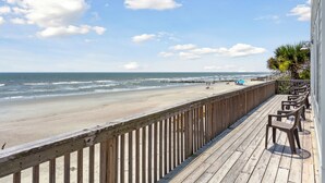 A wooden deck with a view of the beach and ocean.