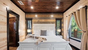 Een slaapkamer met een groot bed, houten wanden, een wit hoofdeinde en een raam met gordijnen.