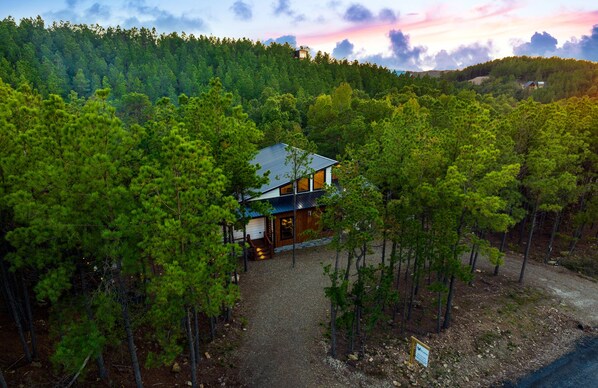 A cabin surrounded by dense forest, with a gravel driveway leading to the entrance. - Pets, Big Deck, Hot Tub, Fire Pit, Mountainside Escape (Broken Bow)