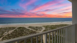 Vue sur la plage depuis un balcon doté d’une balustrade, avec une plage de sable et l’océan en toile de fond.